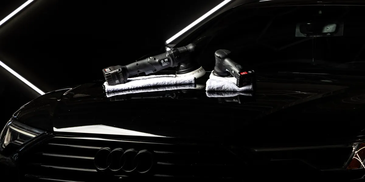 Two cordless Adam's polishers standing on the hood of a black car in a detailing bay
