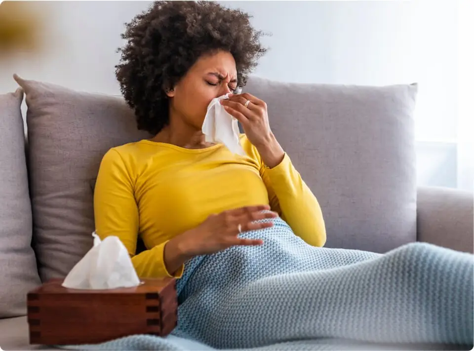 Woman sitting indoors with a box of tissues during allergy season