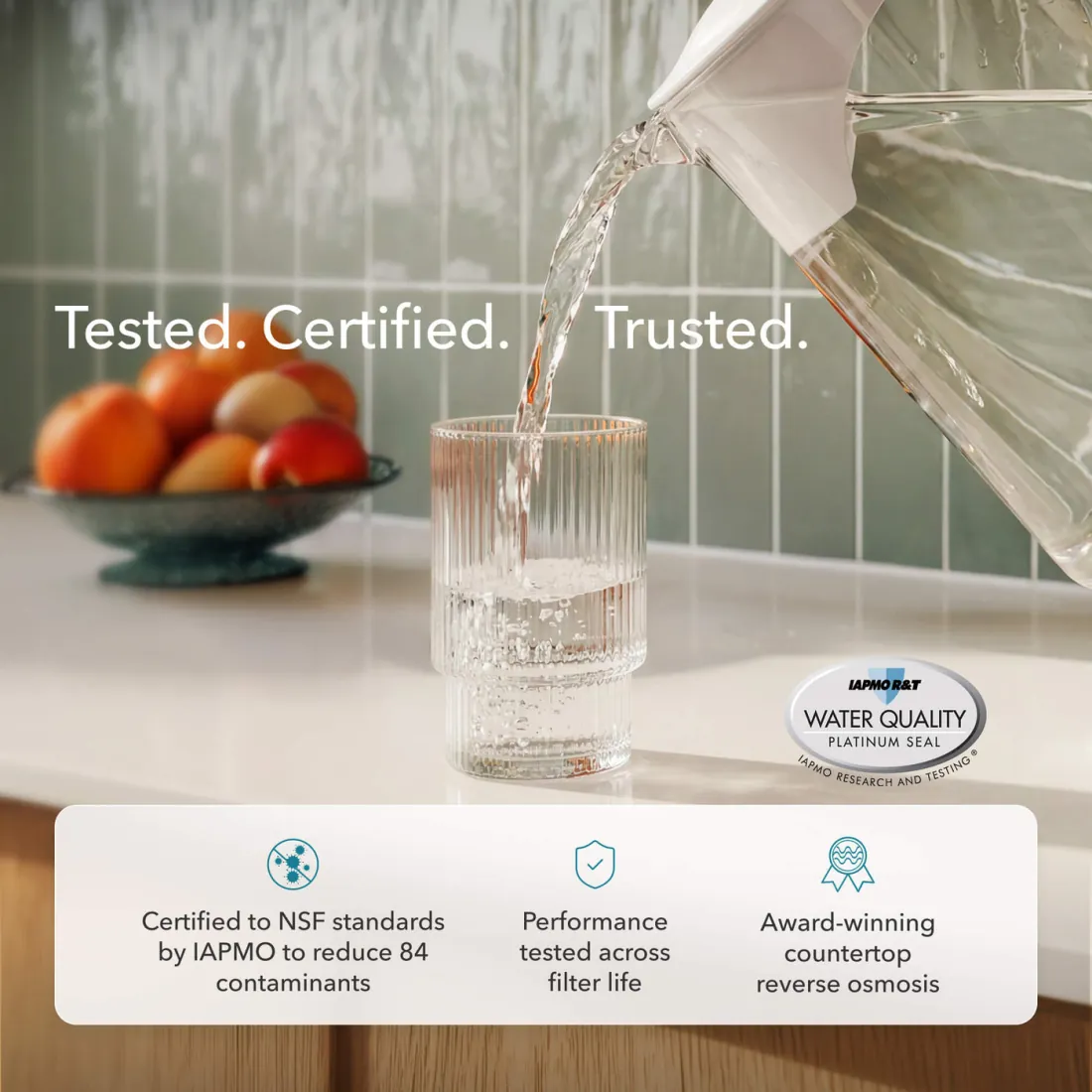 Water poured from an AquaTru carafe into a glass, beside the IAPMO R and T water quality platinum seal