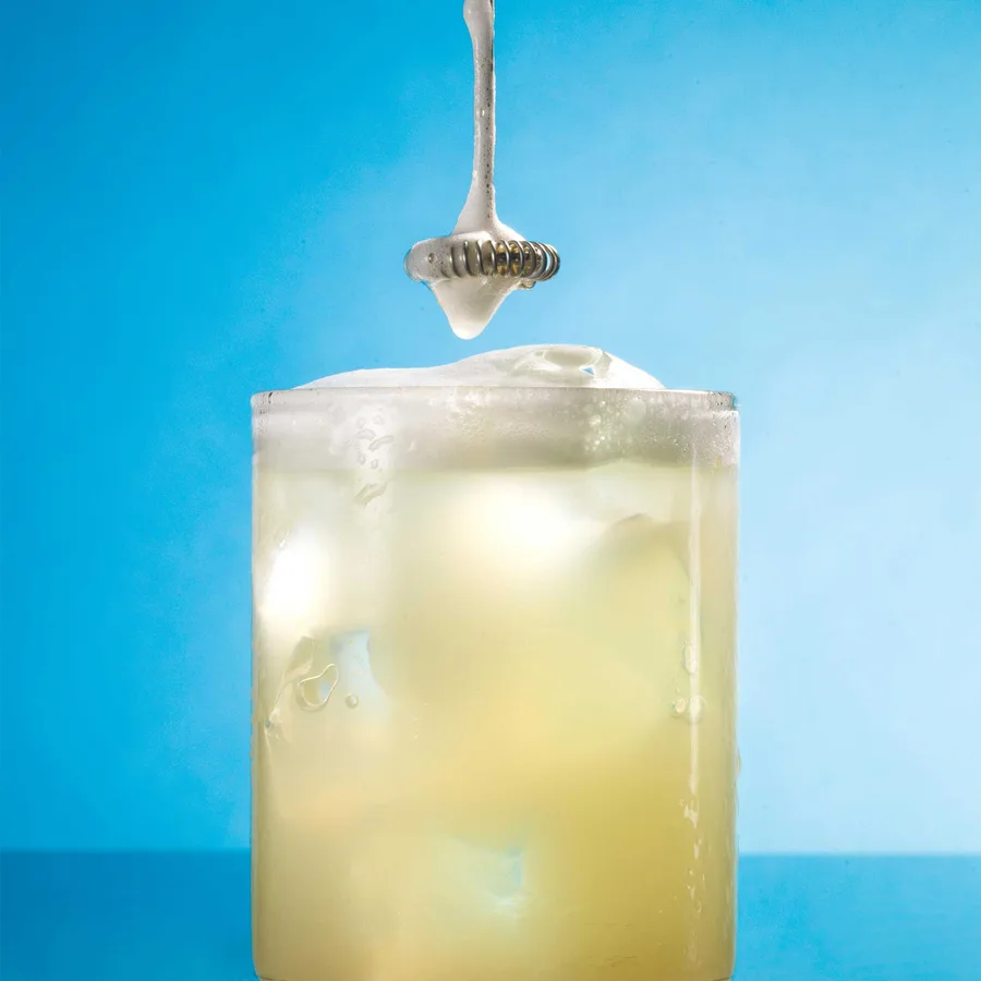 A scoop of ARMRA colostrum being stirred into a cold drink over ice