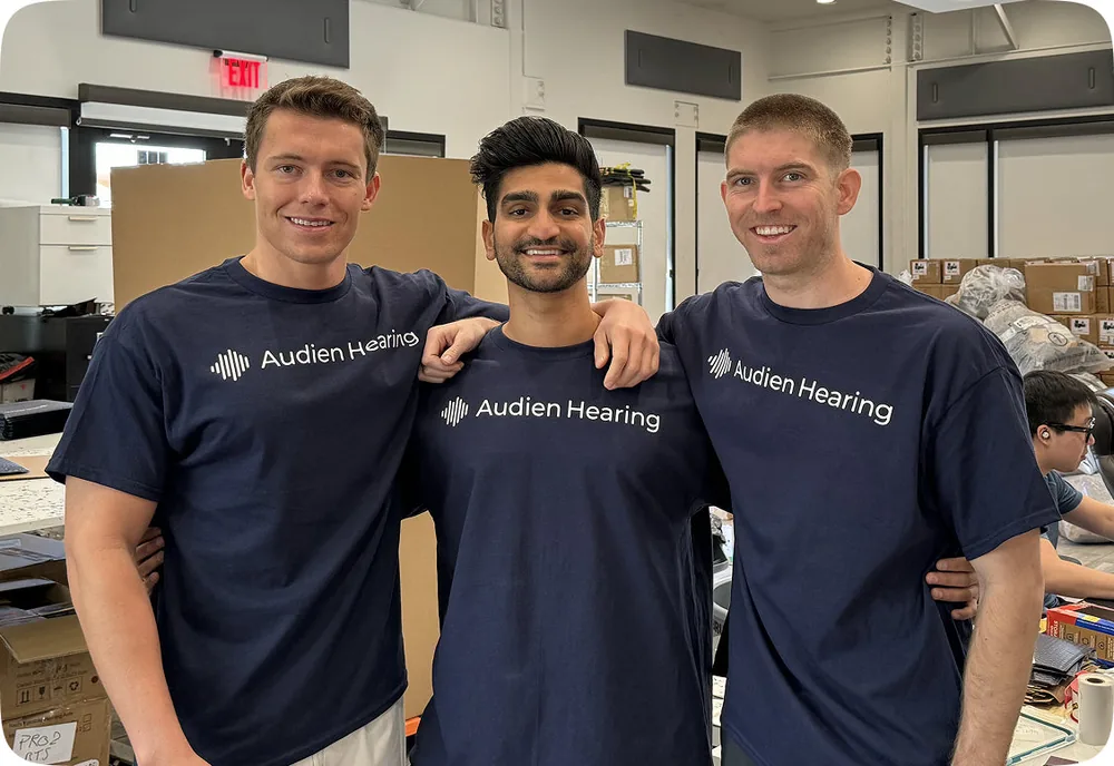 Three Audien Hearing founders in branded t-shirts standing together in the company's office
