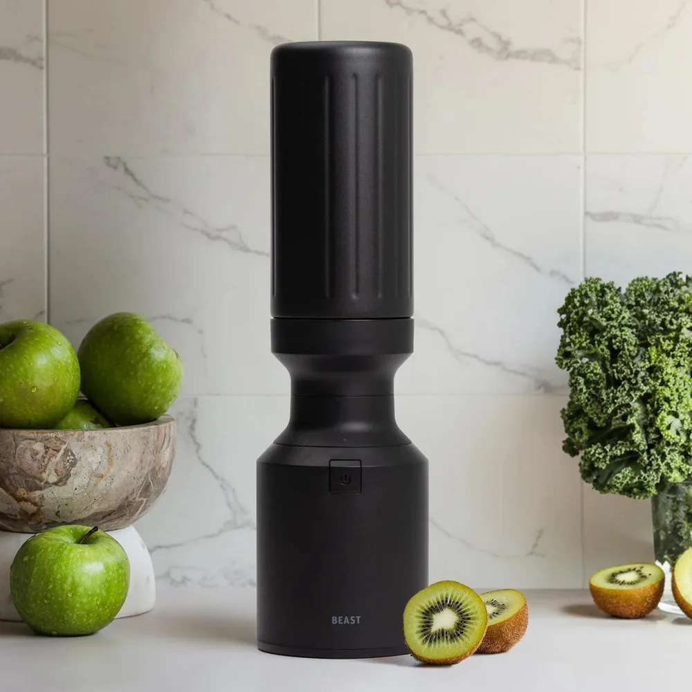 A carbon black Beast blender standing on a kitchen counter beside fruit and greens