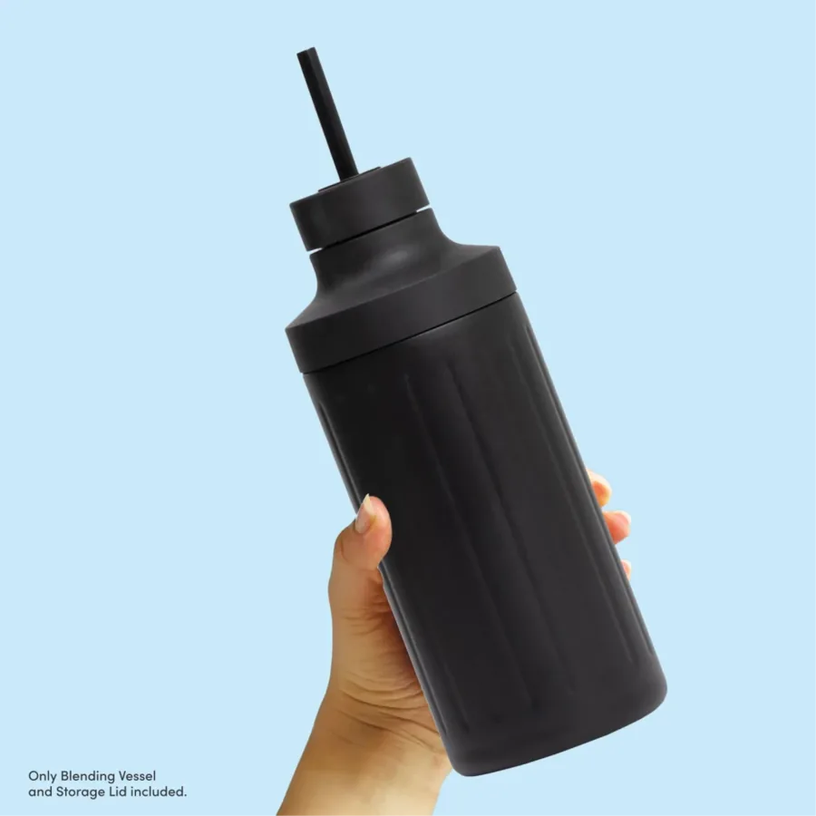 A hand holding a black Beast stainless steel blending vessel fitted with a straw cap