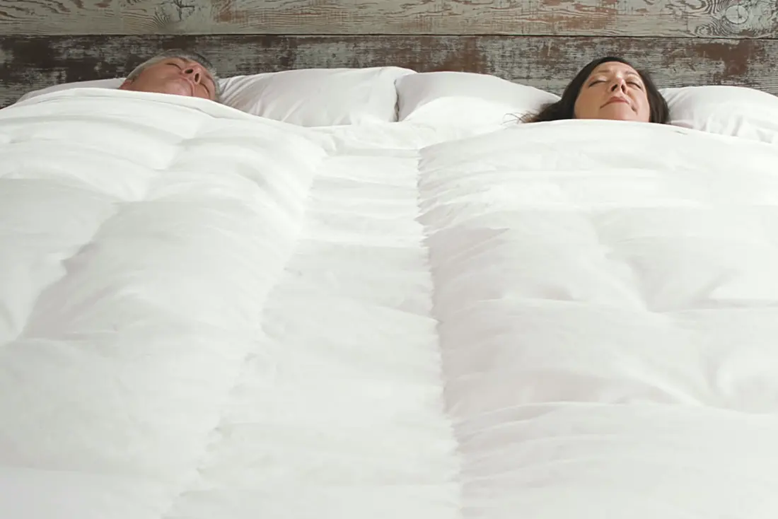 A couple asleep side by side under a single white comforter.
