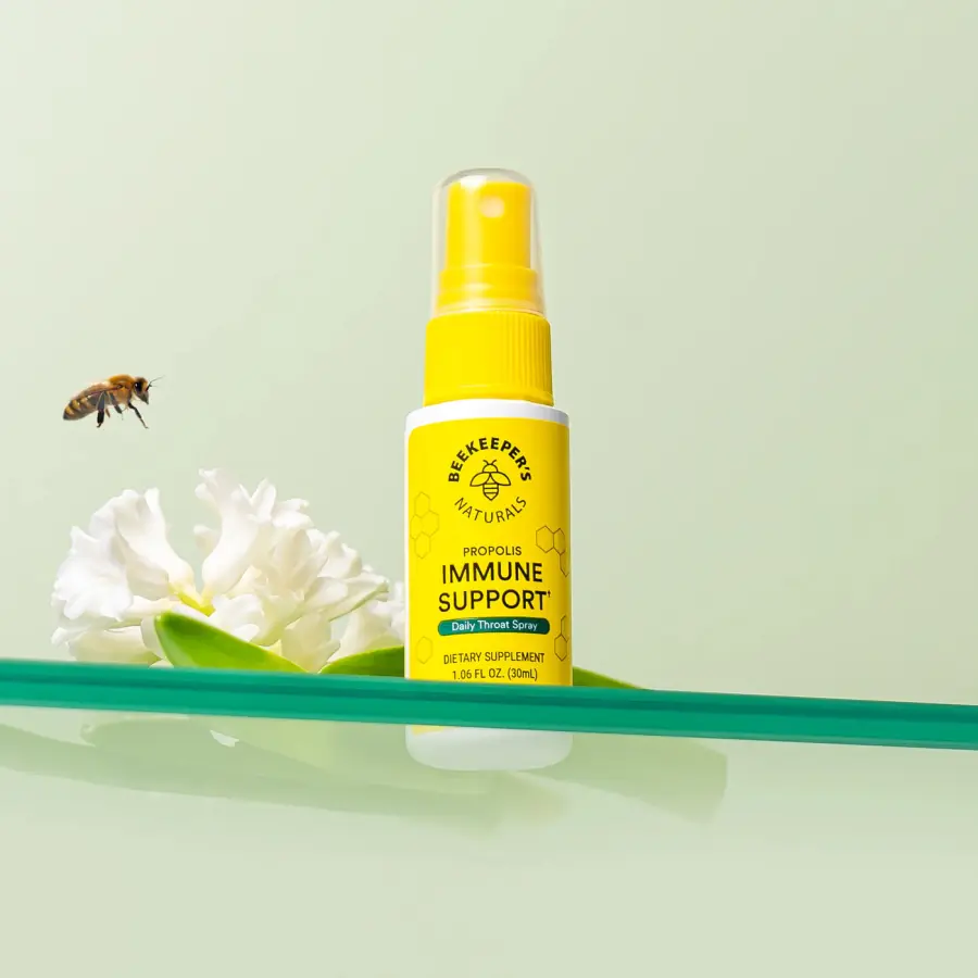 The yellow propolis throat spray bottle resting on a pale shelf with a honeybee nearby