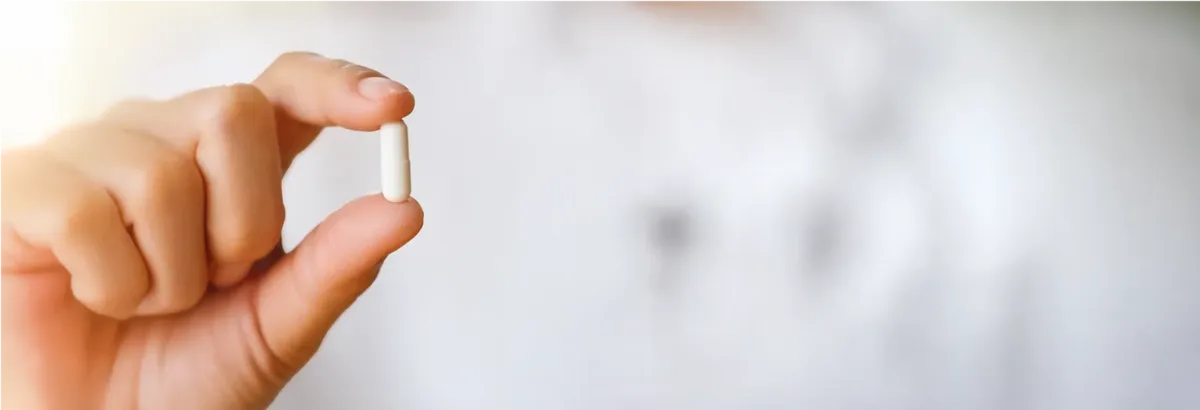 A hand holding a single white Magnesium Breakthrough capsule between finger and thumb