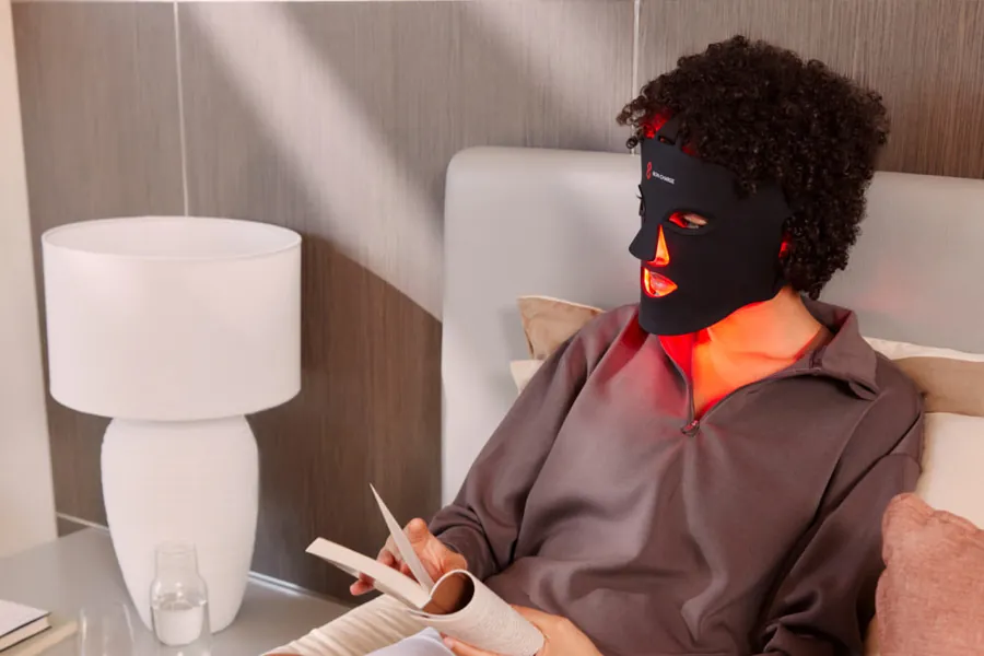 Someone relaxing at home while wearing the BON CHARGE Red Light Face Mask