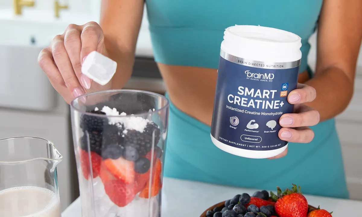 Person adding a scoop of Smart Creatine to a blender with strawberries and blueberries