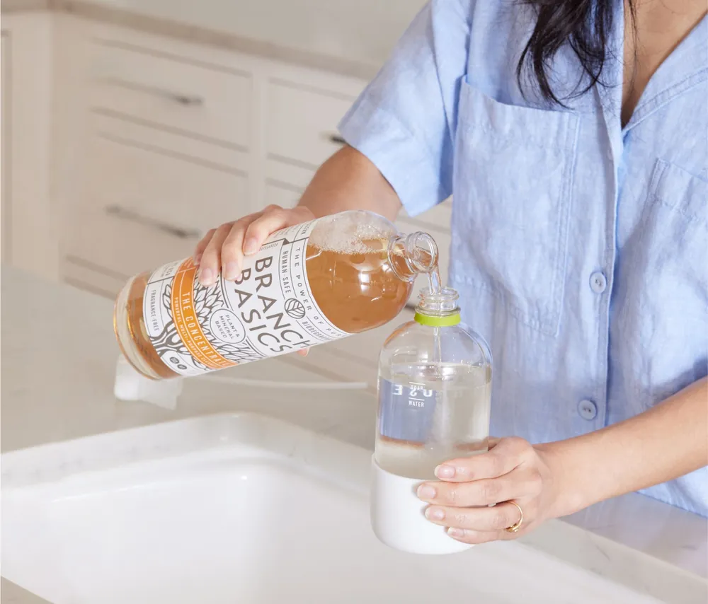 Concentrate being poured into a refillable spray bottle at a kitchen sink