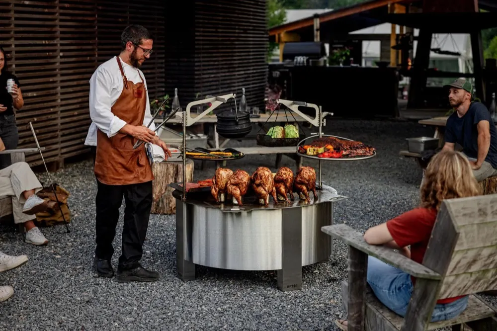 A chef cooking whole chickens on a rotisserie mounted over a large Breeo X42 fire pit