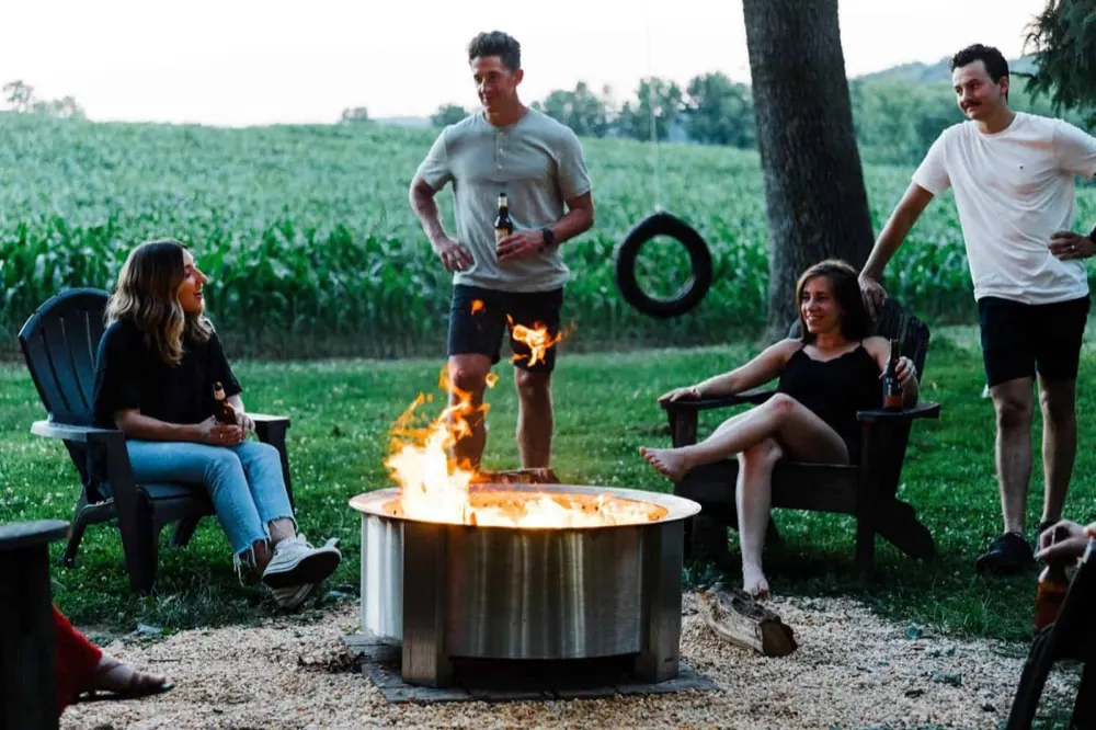 Four friends sitting close around a lit Breeo X30 fire pit in a backyard at dusk