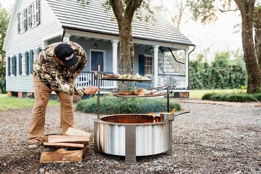 A man cooking on a sear plate fitted to the rim of a Breeo X30 fire pit in front of a house