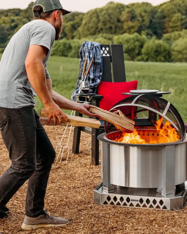 A man dropping split logs into a lit Breeo X19 fire pit