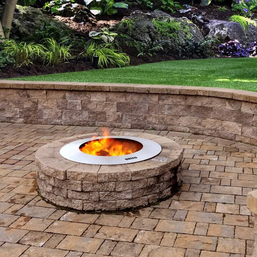 A Zentro stainless steel insert fitted inside an existing stone block fire pit on a paver patio, burning