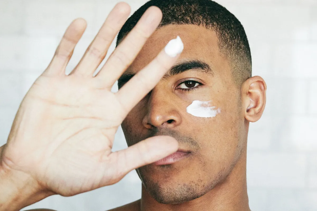 A man applying a small amount of face cream to his cheek, hand raised toward the camera