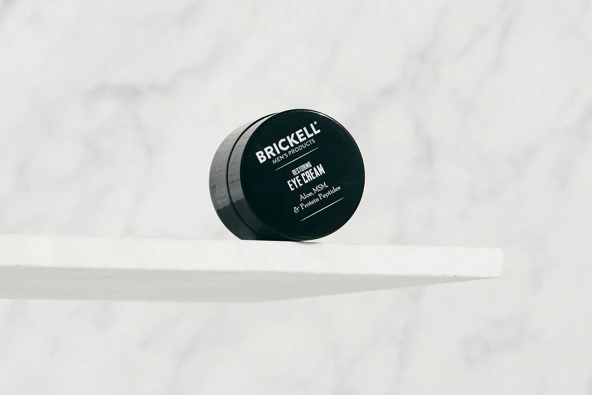 Brickell Restoring Eye Cream jar resting on a white ledge against marble