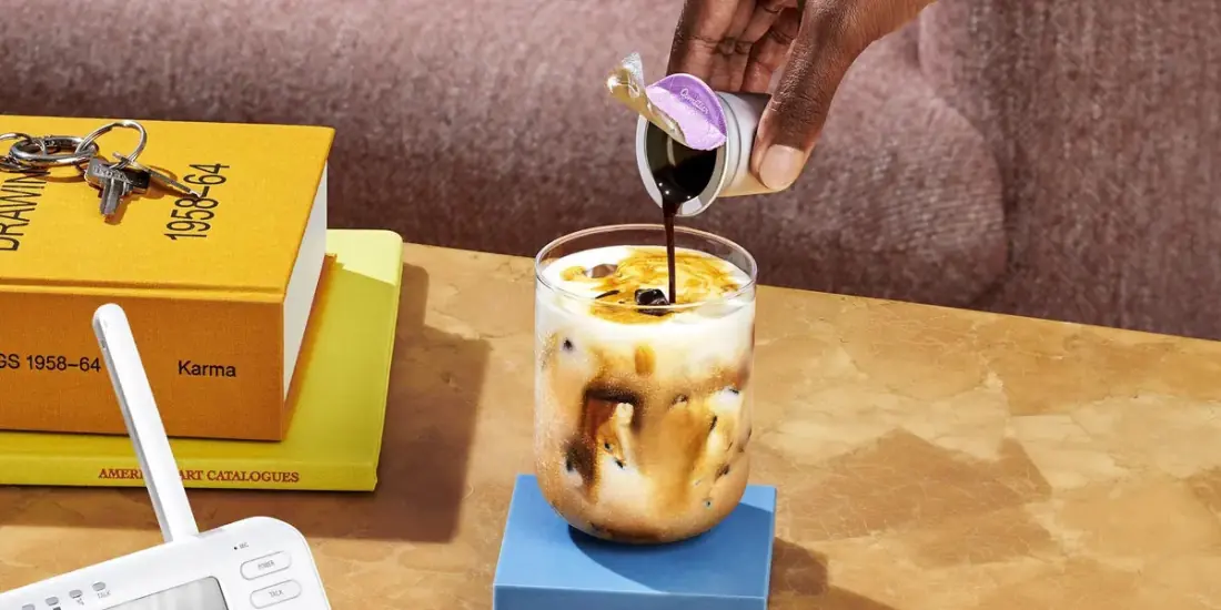 A melted Cometeer capsule being poured into a glass of milk and ice on a side table