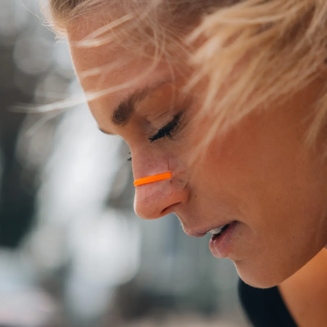 Close-up of a runner mid-effort, head down, wearing a bright orange nasal strip across the bridge of the nose