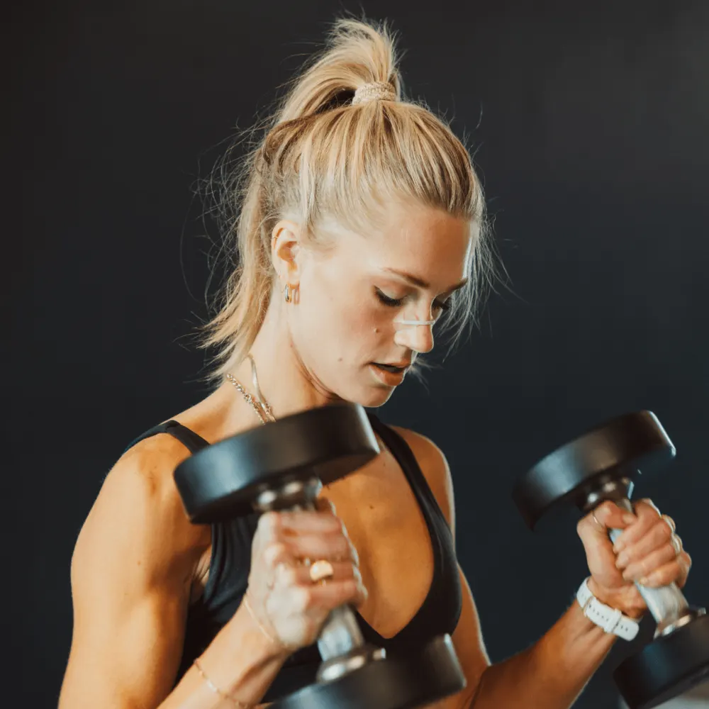 A woman training with dumbbells in a dark gym, wearing a nasal strip
