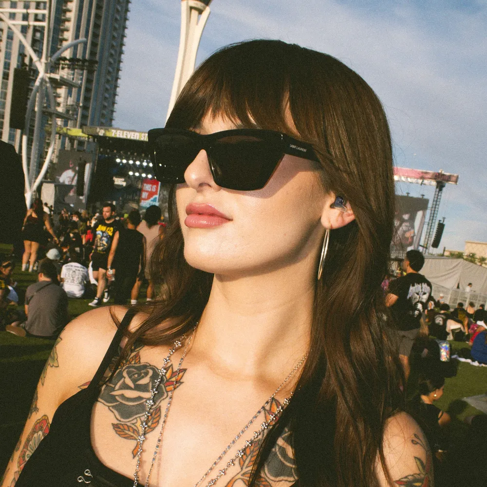 A woman at an outdoor festival wearing dark high fidelity earplugs