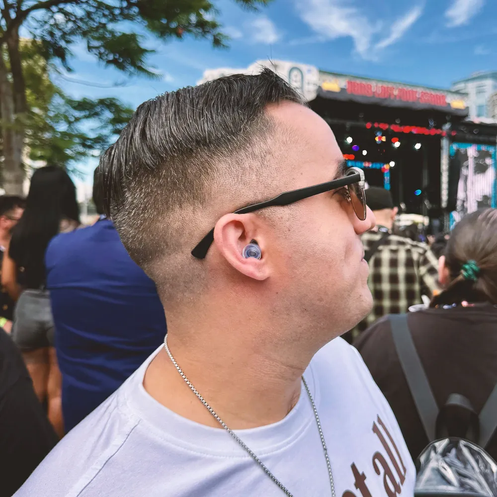 A man at an outdoor daytime festival wearing a filtered earplug