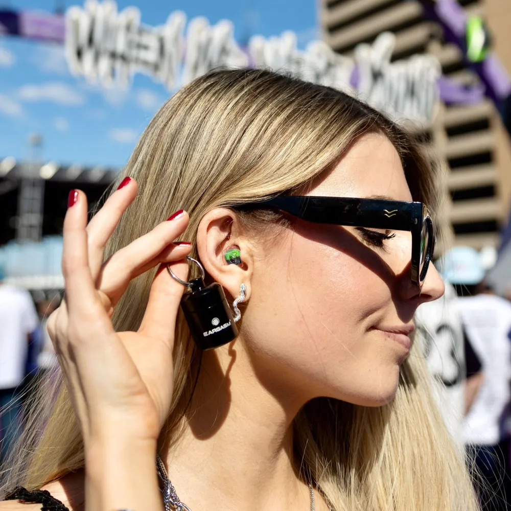 A festival goer in sunglasses wearing filtered earplugs