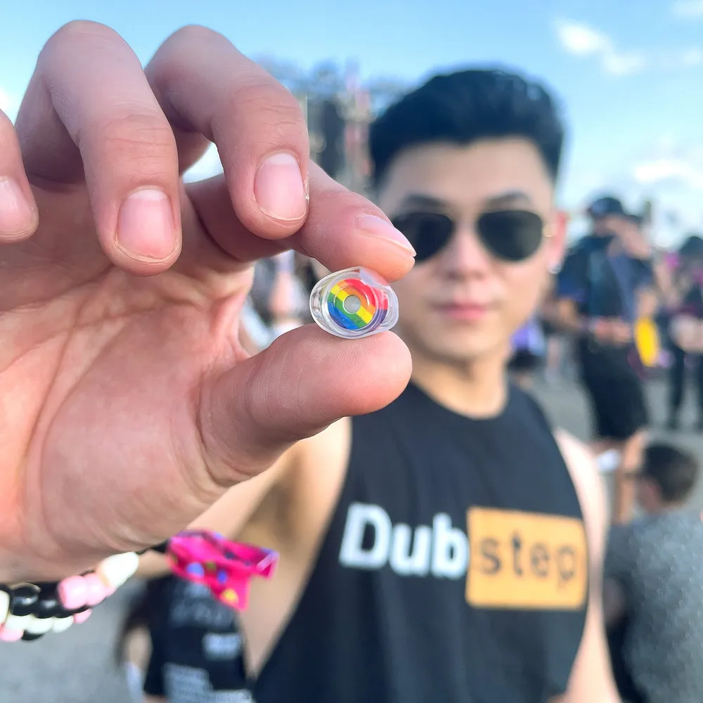 A festival goer holding a pair of rainbow high fidelity earplugs