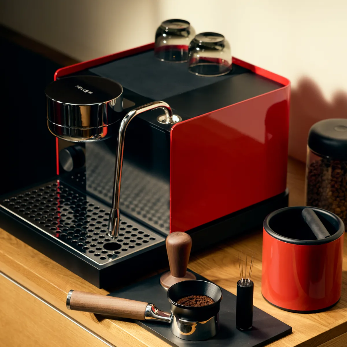 Fellow Espresso Series 1 in Cherry Red on a wooden counter, next to a dosed portafilter, a wooden tamper and a distribution tool