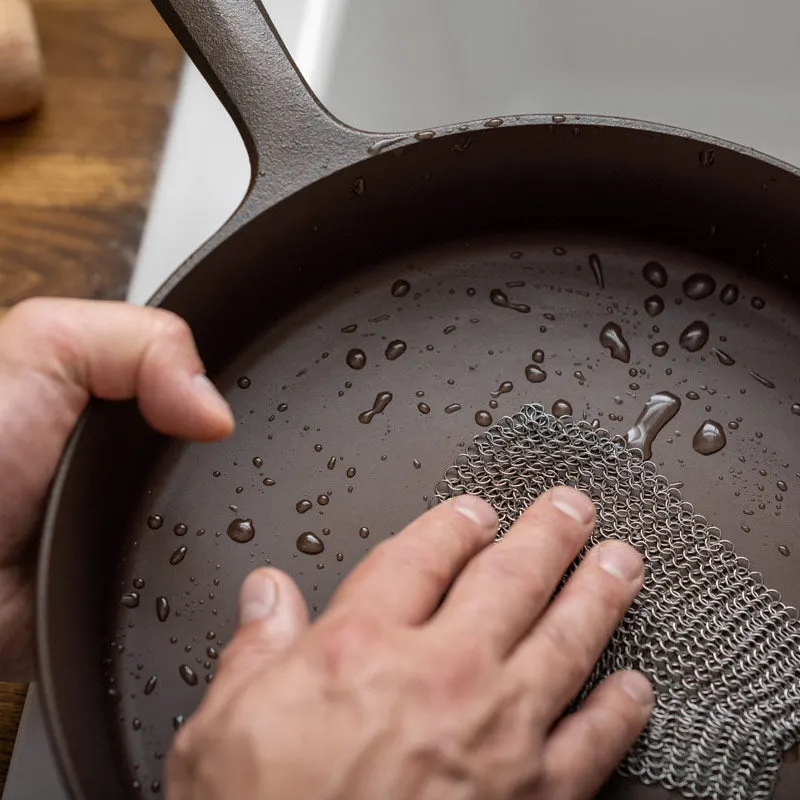 Hands cleaning a cast iron pan under water with a chain mail scrubber