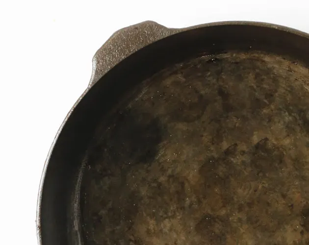 A cast iron cooking surface showing mottled patchy areas where acid has stripped the seasoning