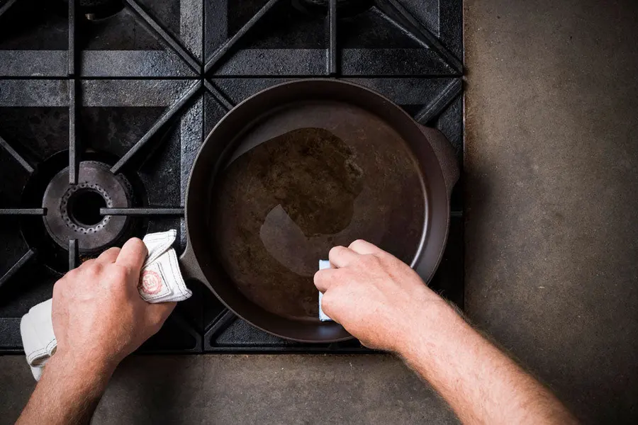 Overhead view of a cast iron skillet being wiped clean on a stovetop