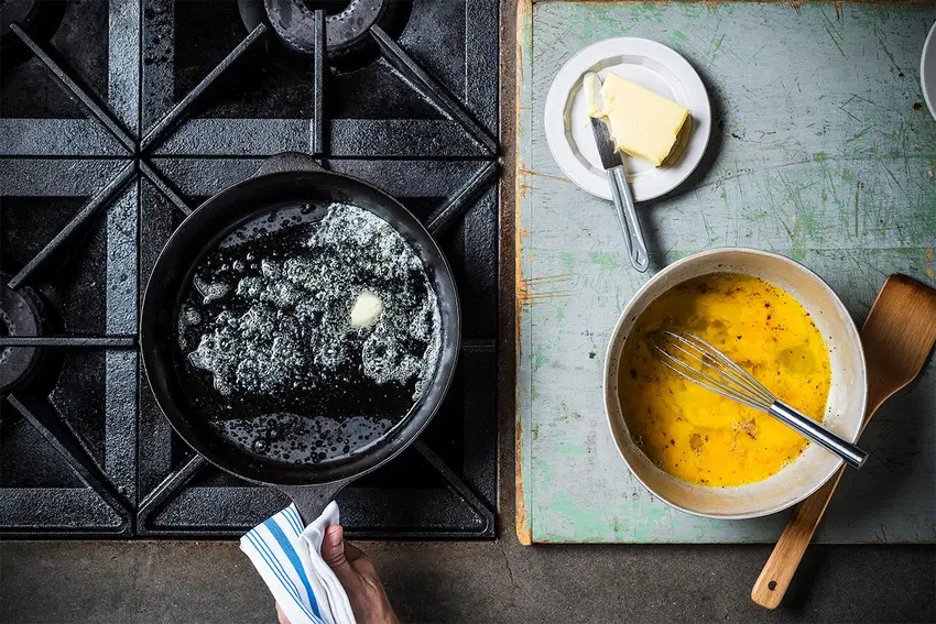 Eggs frying in a cast iron pan with butter and a knob of butter waiting on a board