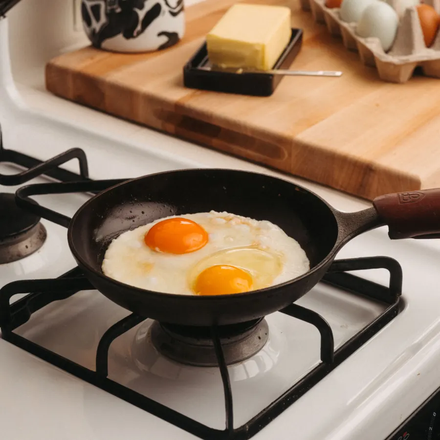 Two fried eggs cooking in a small Field cast iron pan on a white stovetop