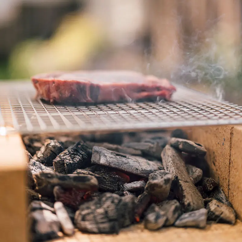 A thick steak searing over glowing charcoal