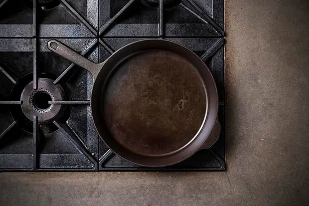 A cast iron skillet on a gas stovetop showing patchy uneven early seasoning