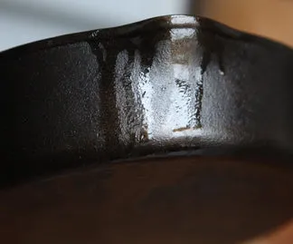 Close-up of grease running down the outside of a cast iron pan below a pour spout