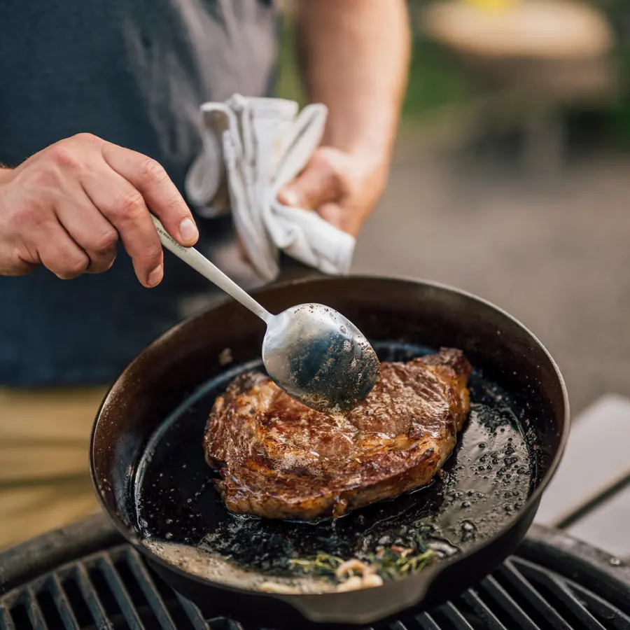 A thick steak searing in a Field cast iron skillet, being basted with a spoon