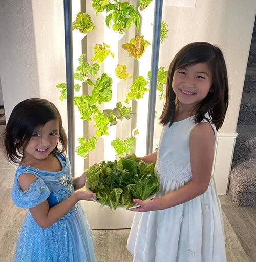 Two children carrying a bowl of greens they have just harvested at home