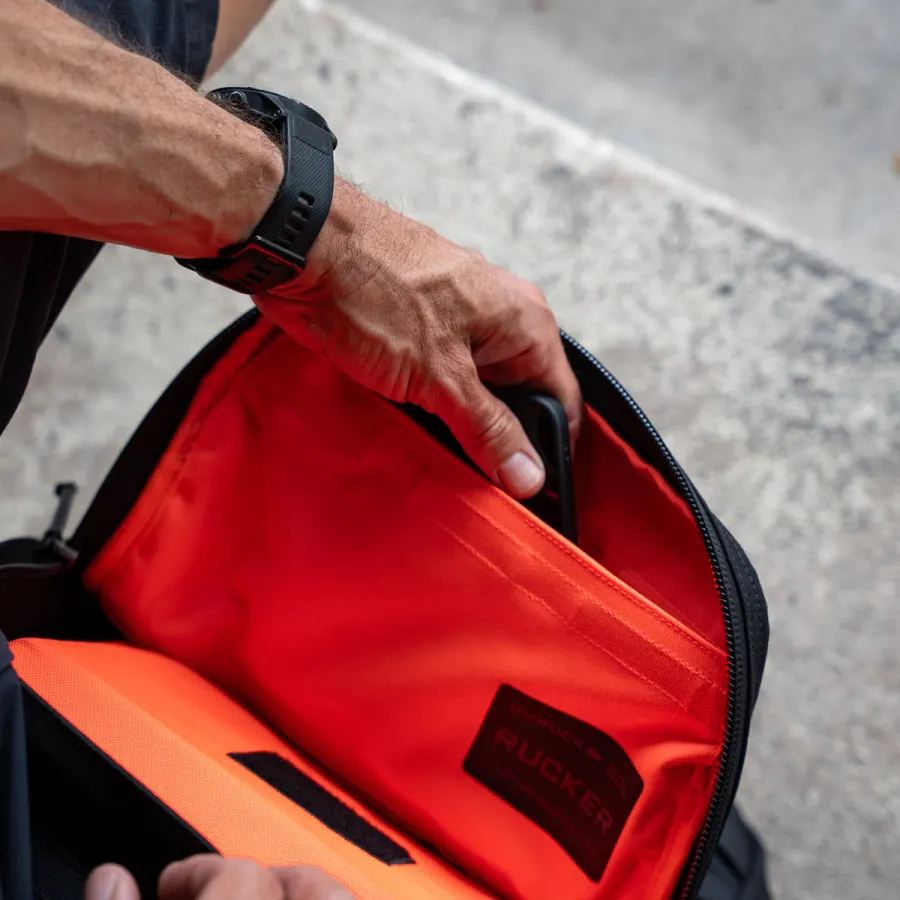 A hand putting a phone into the orange lined interior pocket of a Rucker rucksack