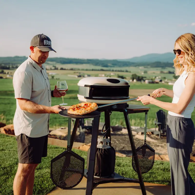Two people serving pizza from a Gozney Arc XL on a stand outdoors.