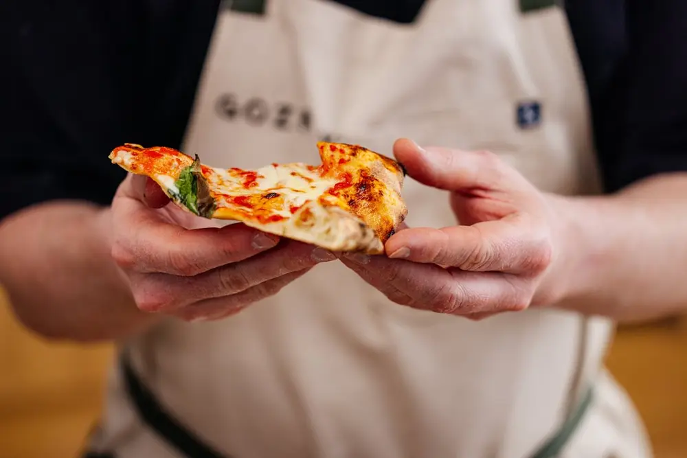 A cook in a Gozney apron holding a folded slice of Neapolitan pizza.