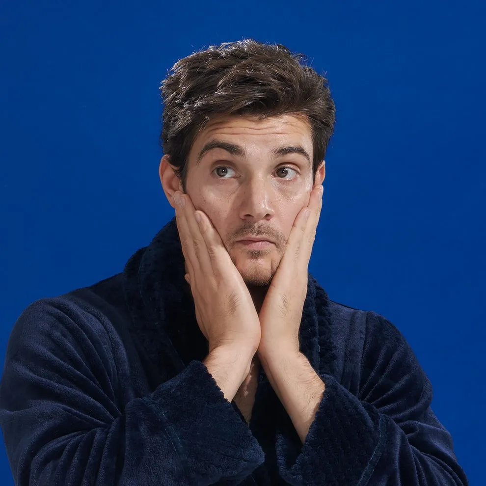 A man in a navy robe pressing his hands against both cheeks