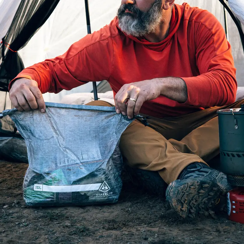 A camper opening a roll-top Dyneema food bag at a camp kitchen.