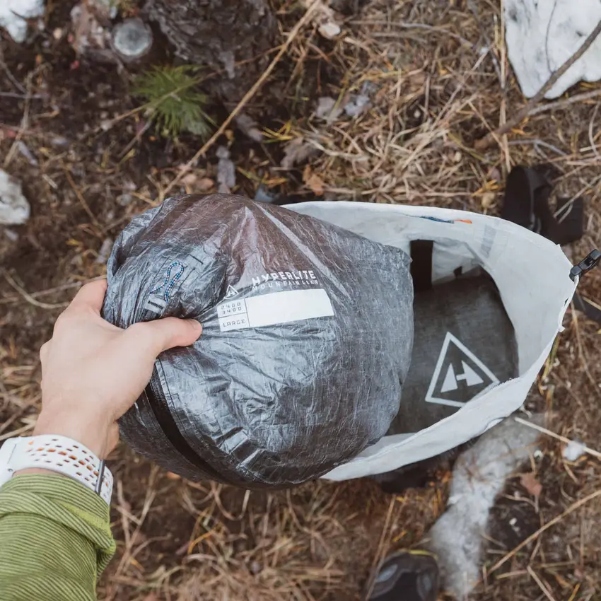 A hand holding a clear Dyneema Pod stuff sack packed with gear, outdoors.