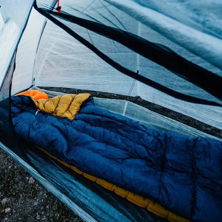 A down quilt laid over a sleeping pad inside a shelter, seen through the mesh door.