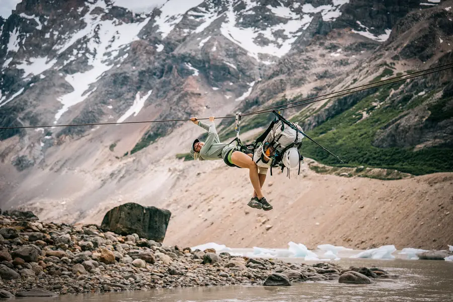 A hiker scrambling down a steep scree slope beside a glacier with a light pack.