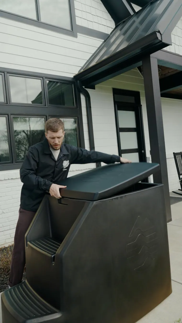 A man opening the lid of an Ice Barrel set up beside a house