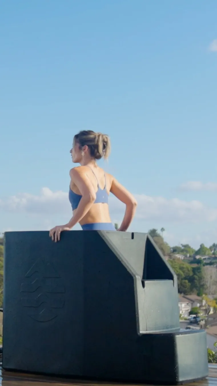 A person sitting in an Ice Barrel outdoors against an open sky