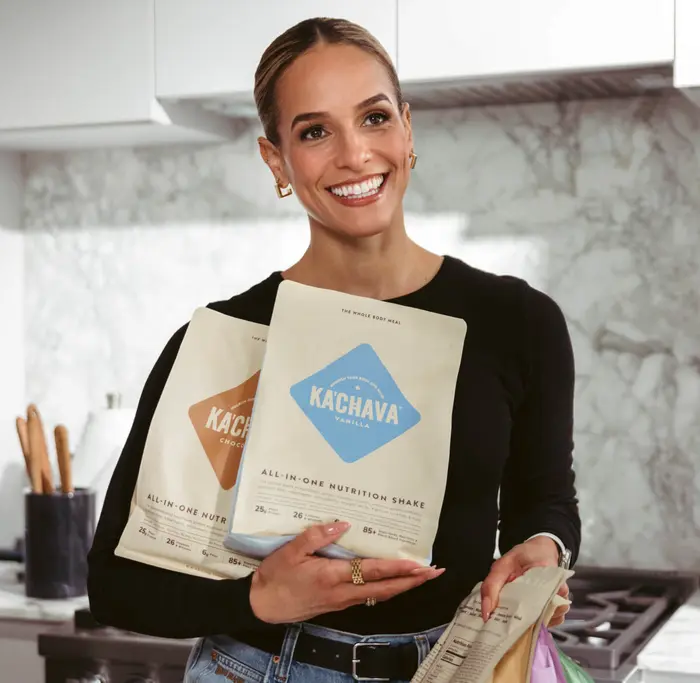 A woman in a kitchen holding several bags of Ka'Chava