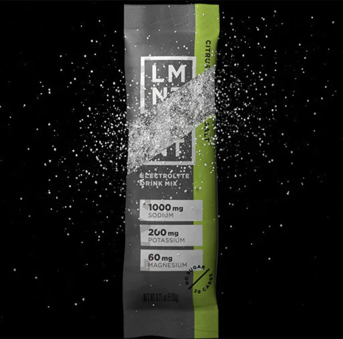 An LMNT Citrus Salt stick pack bursting open with salt against a black background